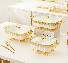 three white and gold dishes sitting on top of a table next to two wine glasses