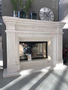 a white fireplace with a clock above it and plants in vases on the mantle