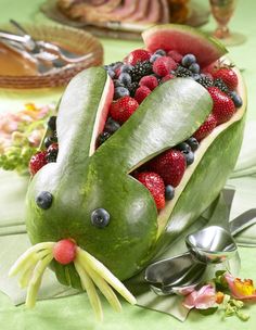 a watermelon shaped like a bunny with berries in it's mouth and spoons to the side