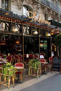 an outdoor cafe with tables and chairs on the side of the street in front of a building