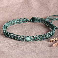 two bracelets with beads and leaves on top of a brown cloth surface next to a feather