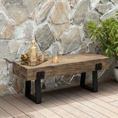 a wooden bench sitting in front of a stone wall next to a potted plant