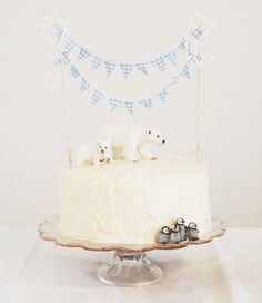 a cake with white frosting and blue bunting on top is decorated with polar bears