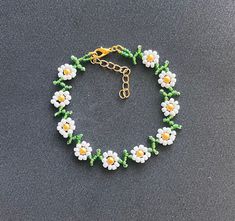 a beaded bracelet with white flowers and green leaves on a black surface, in the shape of a flower