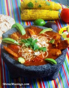 mexican food is served in a bowl with corn and tortillas on the side