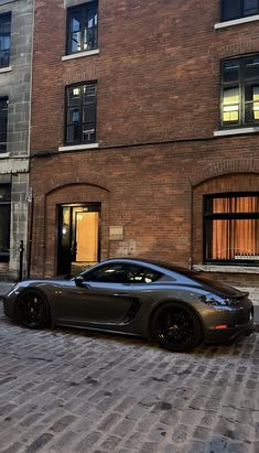 a black sports car parked in front of a brick building on a cobblestone street