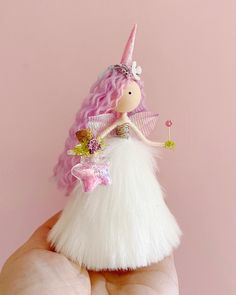 a hand holding a small white and pink fairy doll