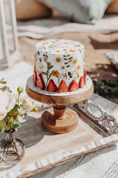 a strawberry cake sitting on top of a wooden tray next to flowers and a vase