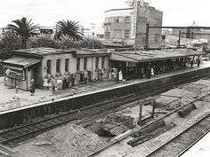 black and white photograph of people standing on the tracks at a train station in an old photo