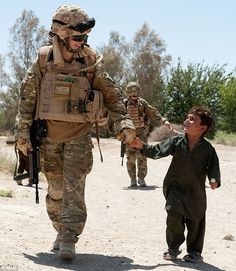 a woman is shaking hands with a soldier in the middle of a dirt road while other soldiers are walking behind her