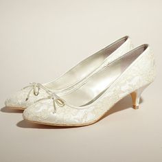 a pair of white wedding shoes with bows on the toe and heel, all covered in lace