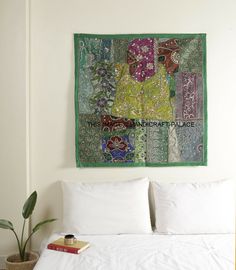 a white bed topped with pillows and a green wall hanging over it's headboard