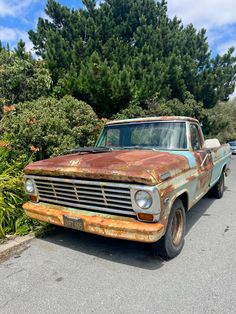 an old rusted truck is parked on the side of the road in front of some trees