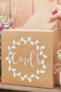 a person holding a card in front of a brown box with white lettering on it