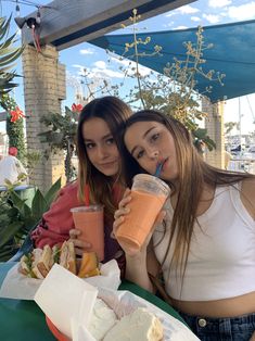 two young women sitting at an outdoor table with drinks and food in front of them