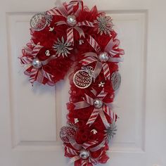 a christmas wreath on the front door decorated with red and white ribbons, silver ornament decorations