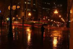 a person with an umbrella standing in the rain on a city street at night time