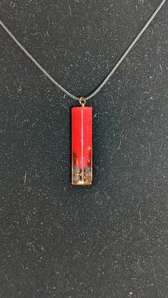 a necklace with a red rectangle shaped object on it's chain hanging from a black surface