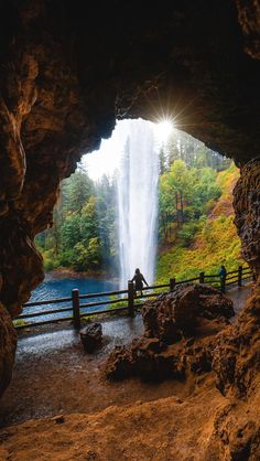 a person standing in front of a waterfall with the sun shining on it's face