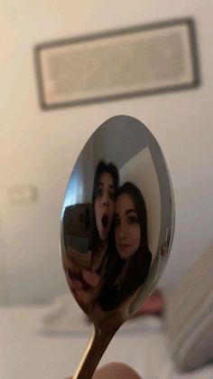 a person holding a spoon with a reflection of two people on it in the mirror