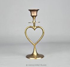 a brass candle holder with a heart shaped design on the top and bottom, standing upright against a white background