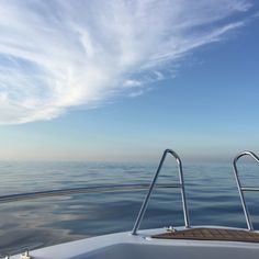 the back end of a boat in the middle of the ocean under a cloudy blue sky