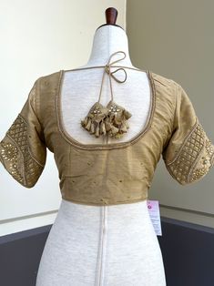 Light Gold Color Raw Silk Readymade Blouse with beautiful Handwork Work. Item : Readymade BlouseLength of the Blouse : 14 inches Length of the Sleeves : 10 inches Color : Light Gold Blouse Fabric : Raw Silk Lining : Yes, it is fully lined Padded or Non-Padded : PaddedClosure: Front Closure with hooks.Ready-to-Wear : YesDisclaimer - : -This is a Standard Size blouse. We do not guarantee perfect fit as every body and shape is different. Little or no alteration would be required to get the perfect Luxury Padded Raw Silk Blouse, Elegant Self Design Top For Navratri, Padded Blouse For Wedding And Transitional Seasons, Festive Self-design Short Sleeve Blouse, Elegant Padded Blouse For Transitional Season, Festival Short Sleeve Self Design Blouse, Gold Unstitched Blouse For Transitional Season, Traditional Short Sleeve Blouse With Zari Work, Long Sleeve Blouse With Resham Embroidery For Navratri