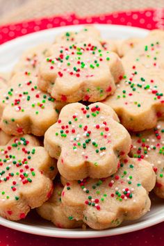 a white plate topped with cookies covered in frosting and sprinkles on top of a red table cloth