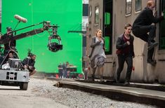 a group of people standing on the side of a train next to a green screen