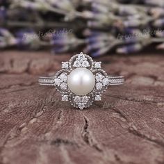 a pearl and diamond ring sitting on top of a piece of wood with flowers in the background