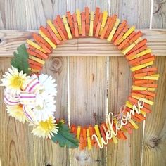 a wreath made out of popsicle sticks with the word welcome painted on it and flowers