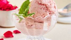 two scoops of ice cream in a glass bowl on a table with rose petals