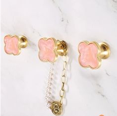 three pairs of pink and gold jewelry on a white marble counter top with two charms attached to it