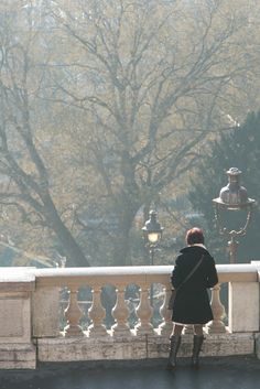 a woman is standing on a bridge looking at the street light and lampposts