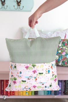 a person is holding a pillow in front of a book shelf with books on it