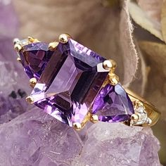 * Fall in love with this classic amethyst ring! The emerald cut amethyst is a deep purple and the nice size of the stone makes a statement all of its own. The center stone has two, trillion cut amethysts that flank either side and two diamonds that give the ring extra sparkle. This ring is elegant and would make a wonderful gift for someone with a February birthday, or anyone with a love for this beautiful gemstone! *  This ring weighs 1.8  grams. This ring tested positive for 14K gold here in o Classic Luxury Multi-stone Amethyst Ring, Luxury Yellow Gold Amethyst Ring, Luxury Multi-stone Gold Amethyst Ring, Luxury Multi-stone Amethyst Ring In Yellow Gold, Luxury Purple Amethyst Ring, Rectangular Shape, Luxury Amethyst Ring Emerald Cut, Elegant Purple Amethyst Baguette Cut Ring, Luxury Emerald Cut Amethyst Ring, Elegant Purple Baguette Cut Amethyst Ring