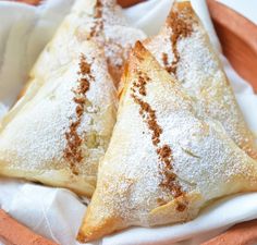 two pastries sitting on top of a paper towel in a wooden bowl with powdered sugar