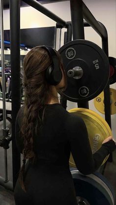 a woman with headphones standing in front of a barbell