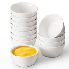 a stack of white bowls next to a bowl filled with yellow liquid on a white surface