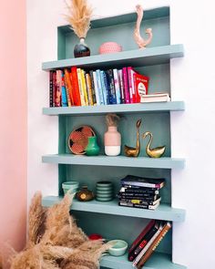 a shelf with books and other items on it in a room that has pink walls