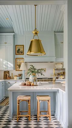 a kitchen with two stools in front of an island and gold pendant light over it