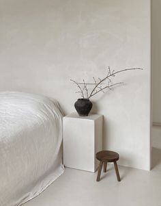 a white bed sitting next to a black vase on top of a wooden stool in a bedroom