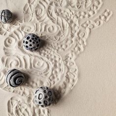 three black and white balls are laying on the sand next to each other in an intricately designed pattern