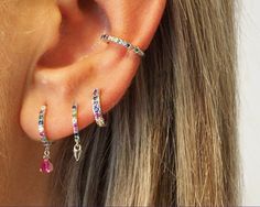 a woman wearing three different colored stones on her ear and one is in the shape of a cross