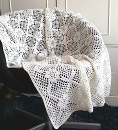 a white crocheted blanket sitting on top of a chair next to a wall