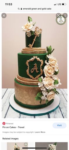 a three tiered green and gold wedding cake with white flowers on top, sitting on a wooden table