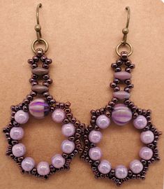 Fatima Earrings in plum have a wreath of round purple beads and larger melon bead. Edges are dark wine seed beads, Stem is made from dusky purple SuperDuo beads and seed beads. They dangle from antique brass jump ring and ball end ear wire. Design by Denise Berryhill of DBBeadingDesigns on Etsy. Created by TLP of Takeen Arts. Item E631. Bohemian Purple Hoop Earrings With Round Beads, Purple Beaded Earrings With Dangling Round Beads, Colorful Round Beaded Earrings, Purple Dangle Beaded Earrings With Spacer Beads, Purple Beaded Oval Jewelry, Handmade Purple Beaded Round Earrings, Purple Beaded Hoop Earrings With Round Beads, Purple Beaded Earrings With Colorful Beads, Purple Beaded Earrings As Gift