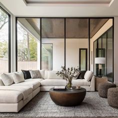 a living room filled with lots of furniture next to tall glass windows on the wall