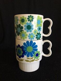 two coffee cups with blue and green flowers on the bottom, one has a heart shaped handle