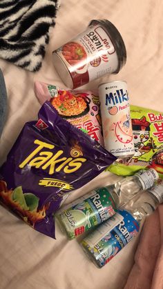 the person is laying in bed with many snacks and drinks on it's side